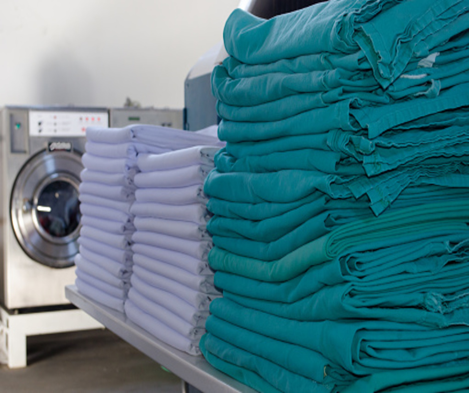 Stack of white sheets and green surgical cloths in an industrial laundry. Cleaning service for hospitals and clinics. Selective focus.